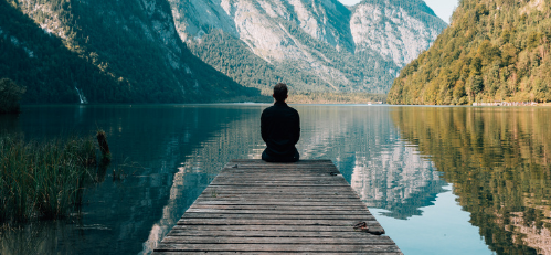 Male sat at the end of a platform with river and mountains